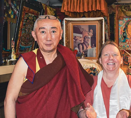 A smiling traveler from England poses with a Buddhist monk inside a traditional temple. This personal interaction is a highlight of a Tibet tour from the UK.