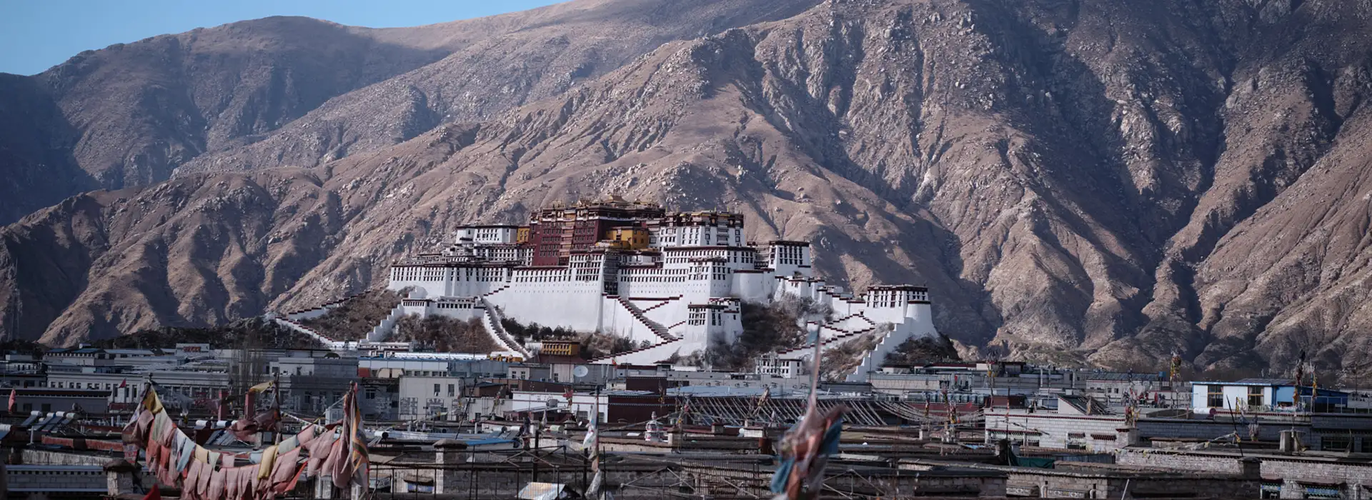 The Potala Palace stands majestically against a backdrop of barren mountains in Lhasa. This historic landmark is a primary stop on a Tibet tour from the USA.