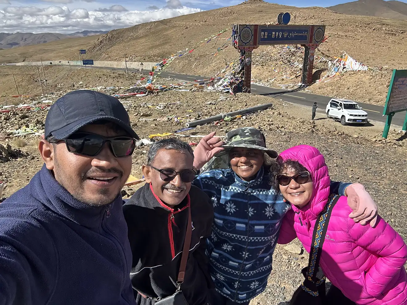 Four happy travelers take a selfie on a high mountain pass with prayer flags. This shared group experience is a key part of a budget Tibet tour.