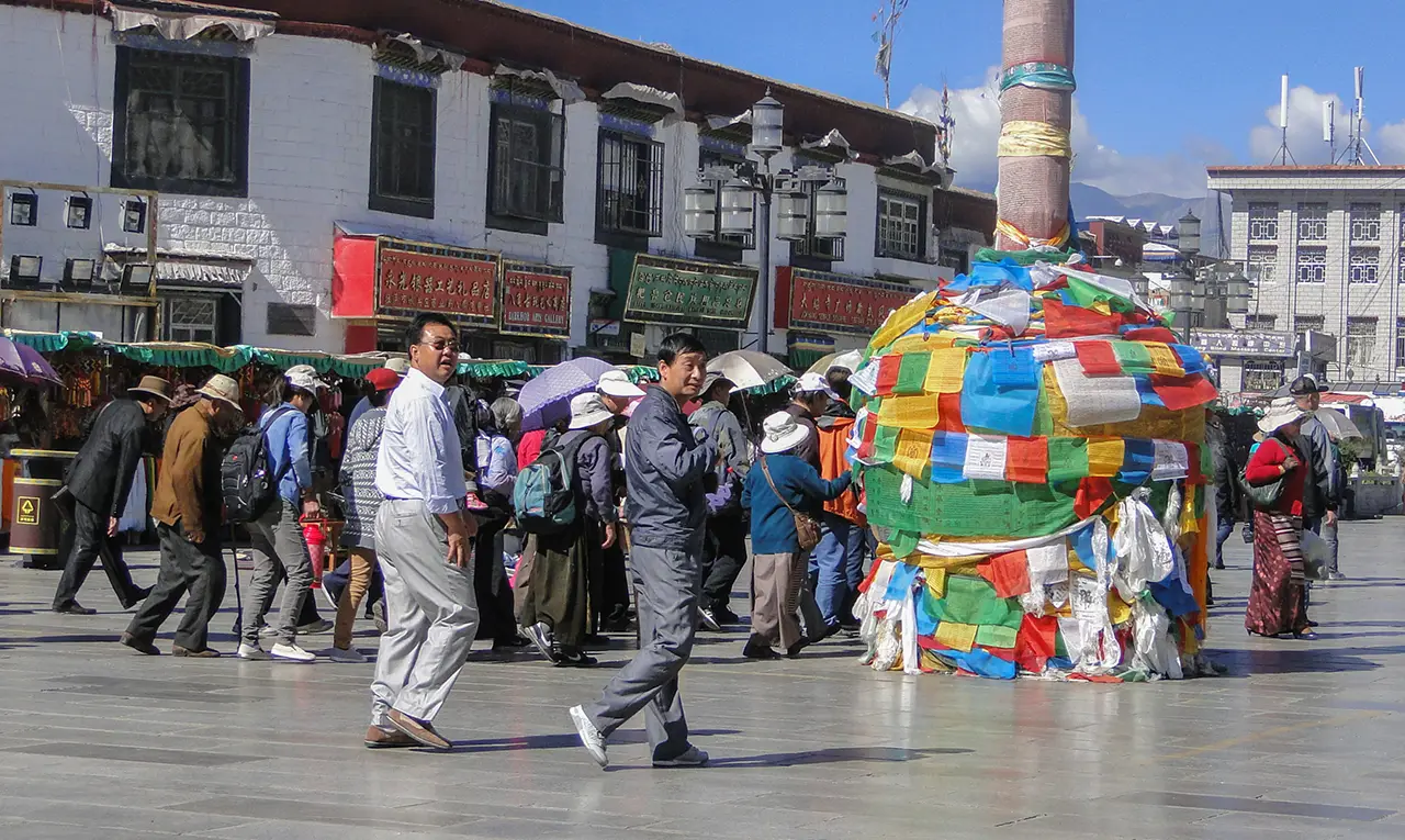 Pilgrims and visitors walk around a colorful prayer flag pole in Barkhor Square near Jokhang Temple in Lhasa, Tibet.