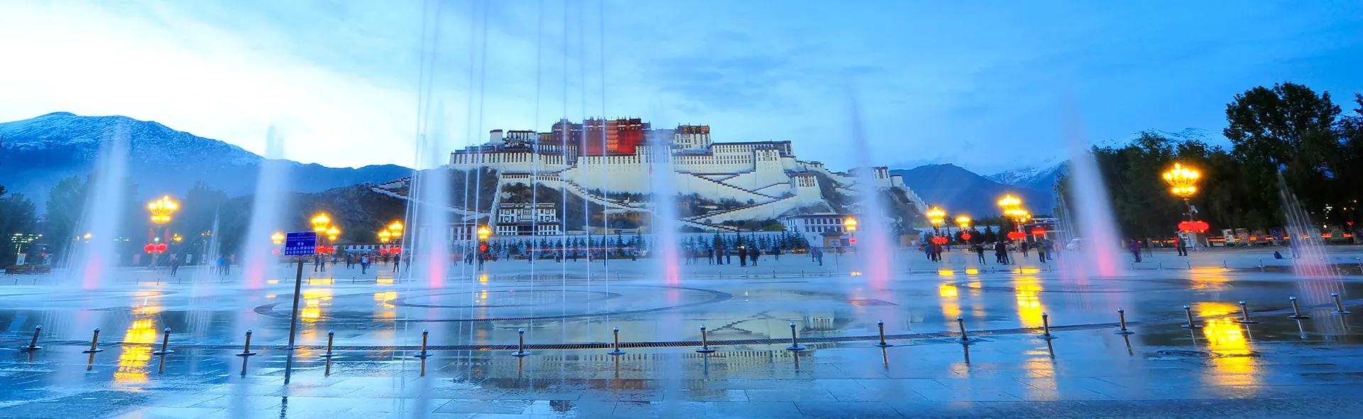 A panoramic evening view of the illuminated Potala Palace across a grand plaza with dancing fountains, highlighting the cultural majesty of Tibet Tour Packages.