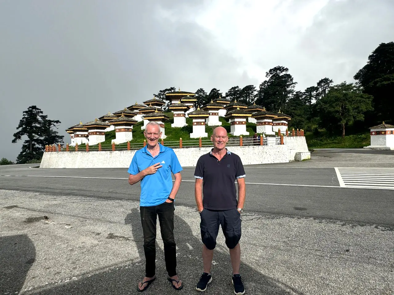Two men standing in front of the 108 memorial chortens at Dochula Pass, illustrating the cultural depth of Bhutan Tour Packages.