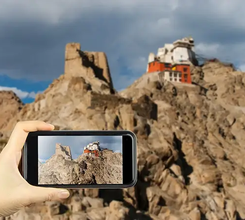 How to Get to Tibet: Best Travel Routes shown through a smartphone capturing a Tibetan monastery and ancient fortress on a rocky hill