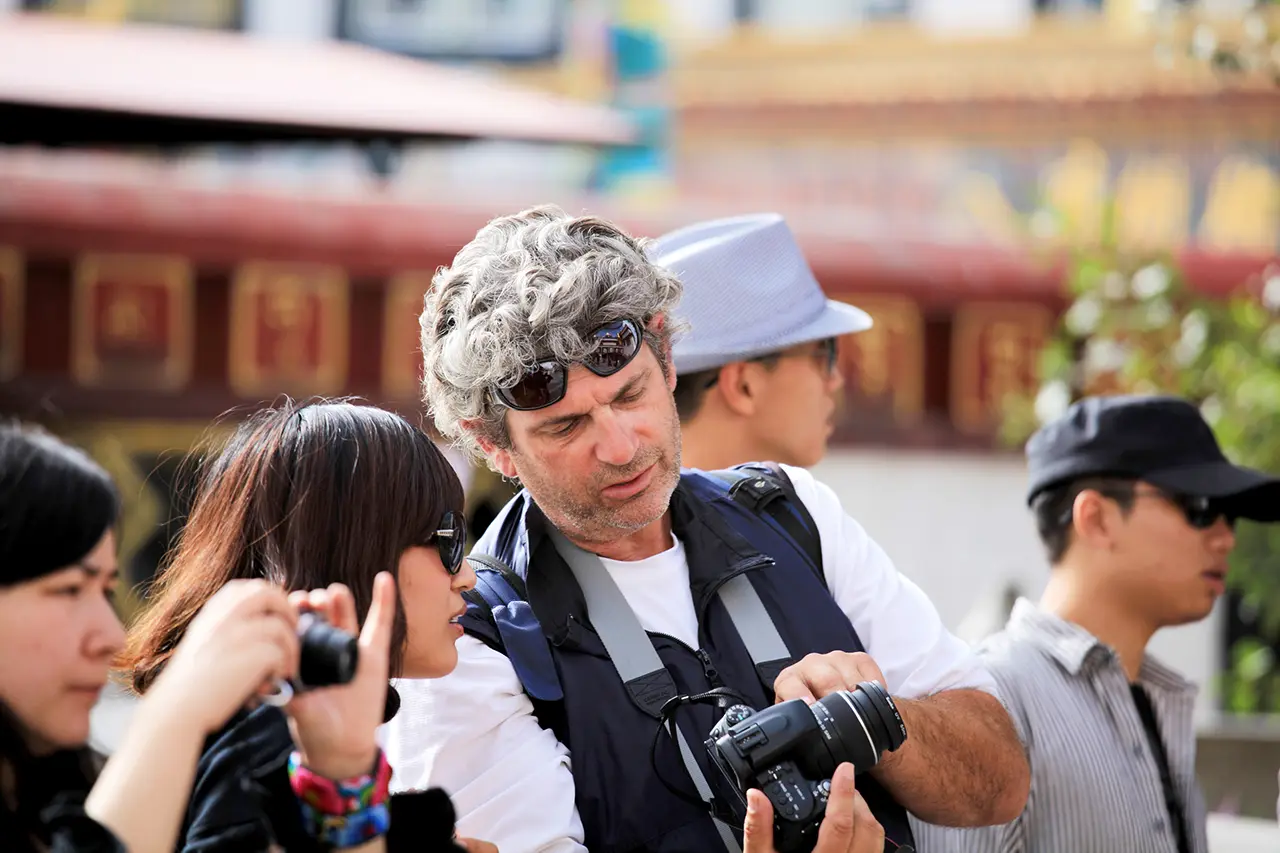 Tourists reviewing photos on a camera while visiting a Tibetan temple courtyard during a guided cultural tour in Lhasa.