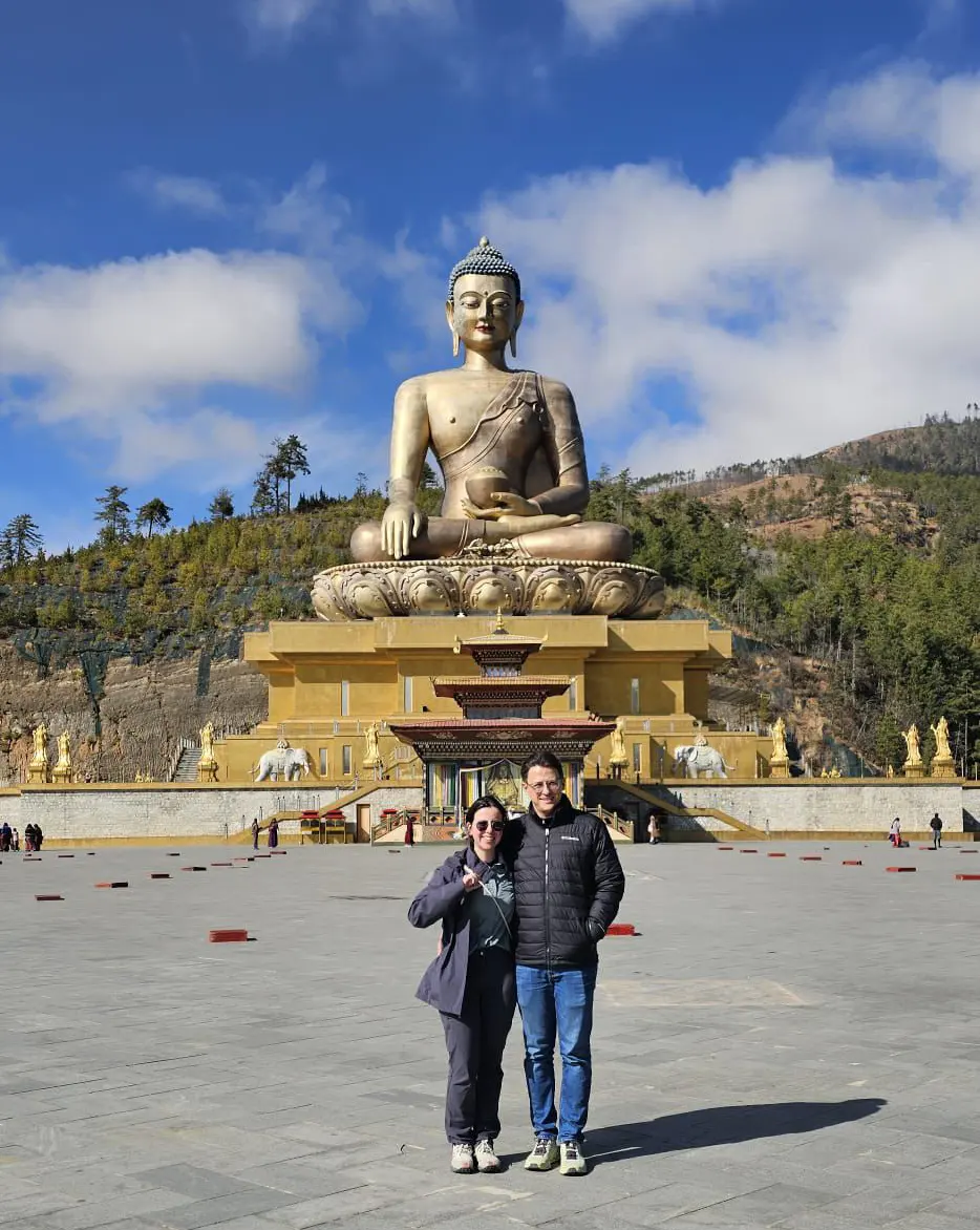 A honeymoon couple posing in front of the giant golden Buddha Dordenma statue in Thimphu, included in cultural Bhutan Tour Packages.