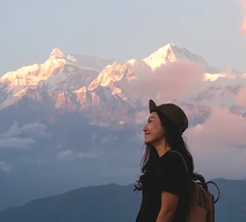 A female traveler smiling while looking at the sunset-lit peaks of the Annapurna massif from Sarangkot, highlighting why October is the best time to visit Nepal.