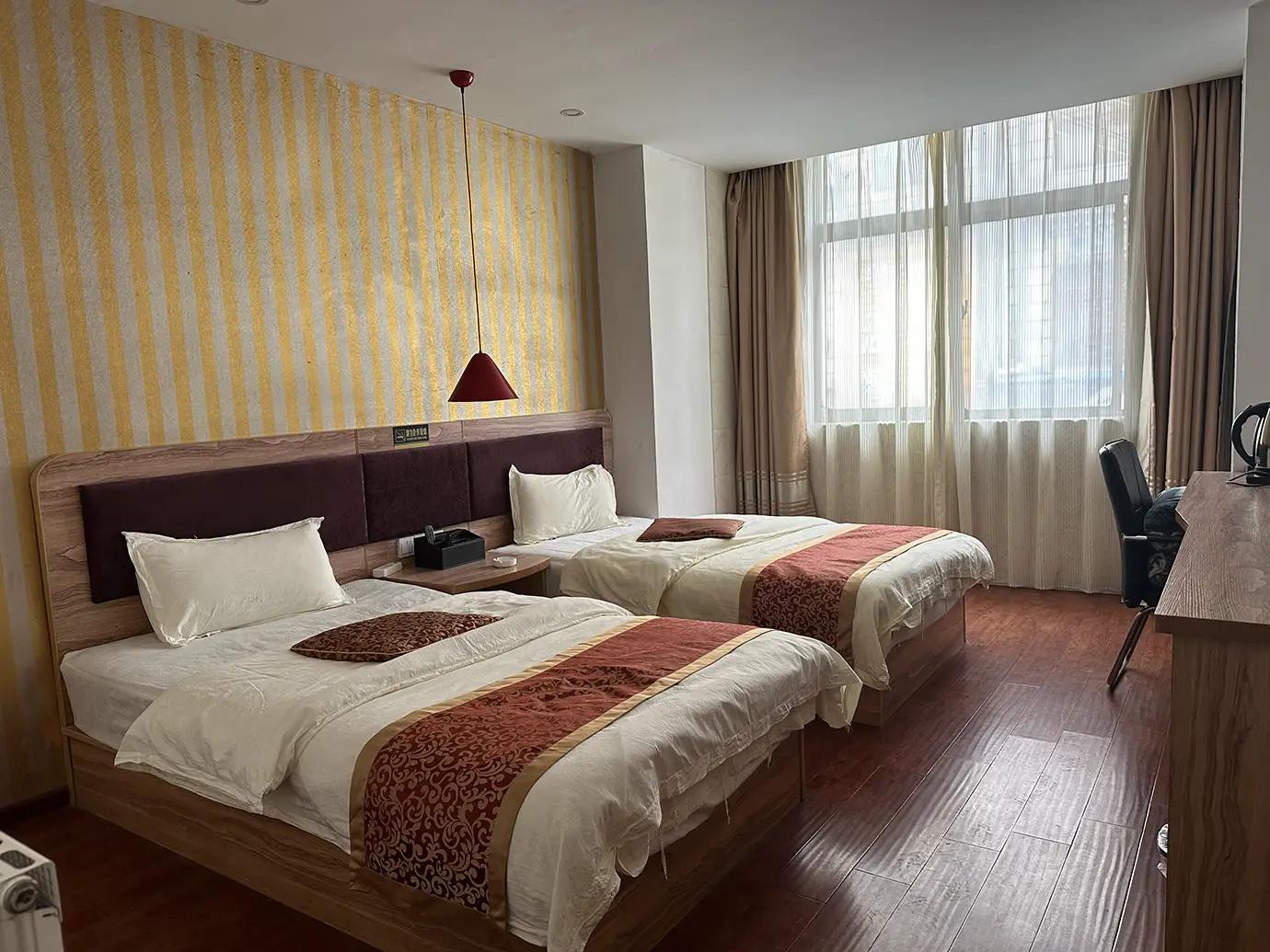Twin hotel room setup during a Tibet Private Tour vs Group Tour, showing standard shared accommodation with two beds, a desk, and a bright window.