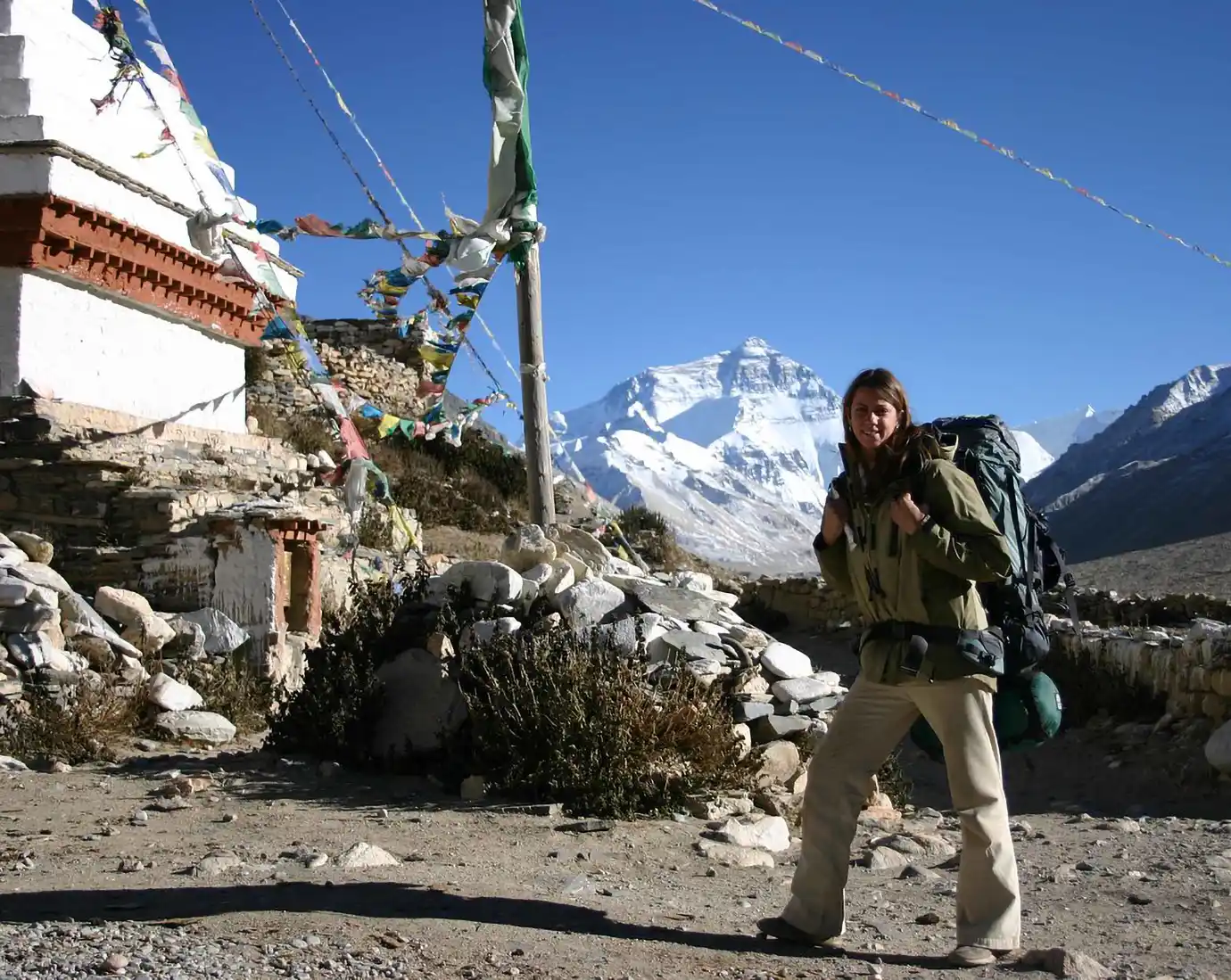 Backpacker stands near prayer flags and a mountain trail with Mount Everest in the background during a Tibet adventure tour across the Himalayan plateau.