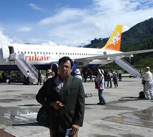 Traveler standing at Paro International Airport beside a Druk Air aircraft, highlighting secure arrival procedures that support Bhutan Travel Safety for international visitors.
