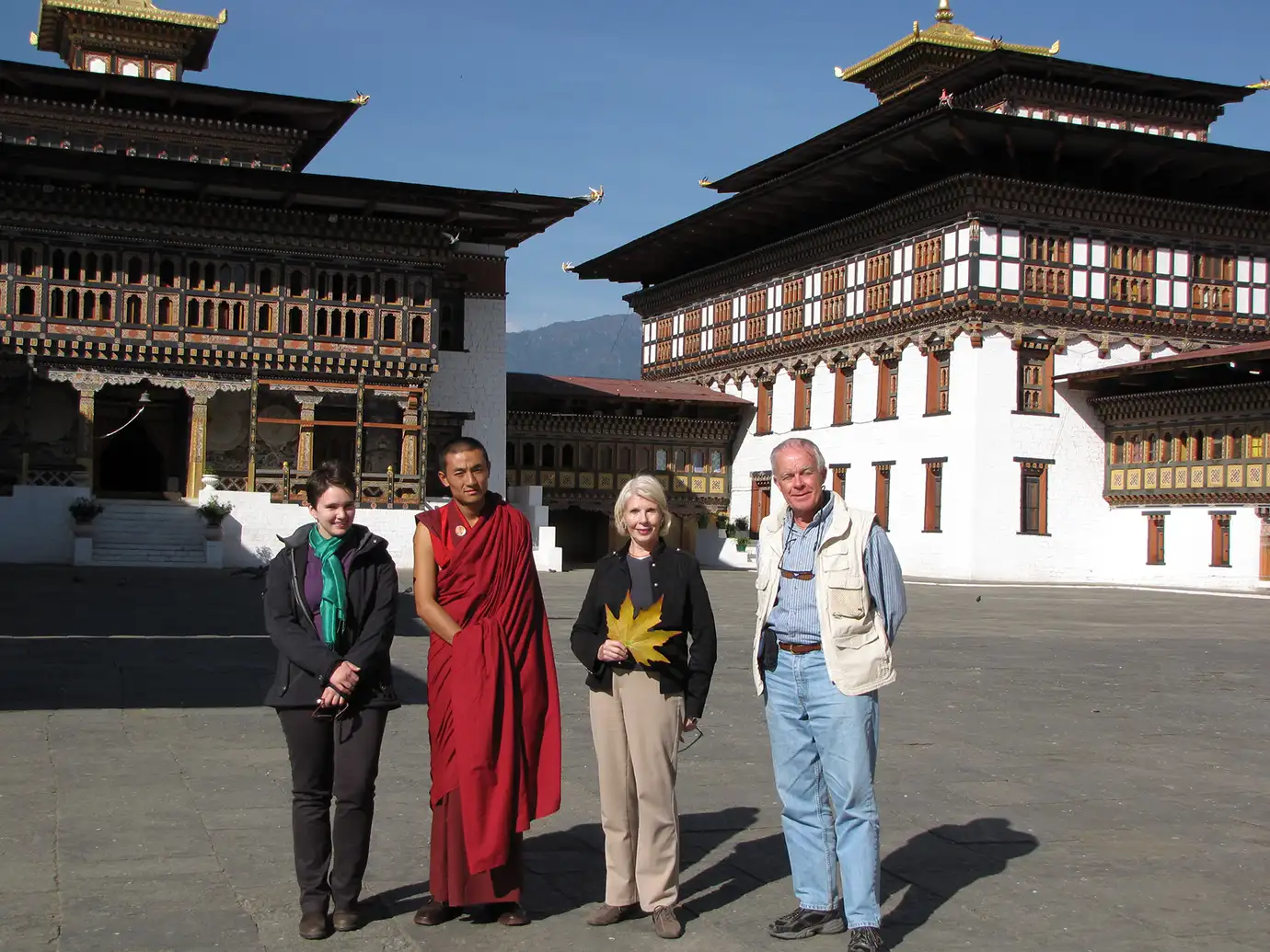 Travelers standing with a Buddhist monk inside a traditional Bhutanese dzong courtyard, highlighting cultural sightseeing experiences where Bhutan Travel Insurance supports safe and well-prepared international travel.