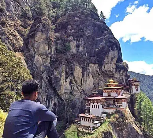 Traveler viewing Tiger’s Nest Monastery perched on a cliff in Bhutan, illustrating high-altitude hiking conditions travelers prepare for with a Bhutan Travel Packing List.