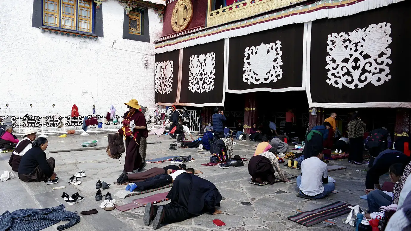 Devout pilgrims perform prostrations on the stone courtyard of a monastery in Lhasa, a deeply moving spiritual scene on a Tibet Buddhist Pilgrimage Tour.