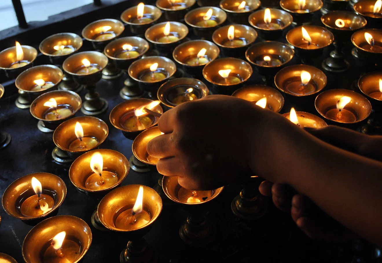 Hands light rows of golden butter lamps during a sacred Tibet festival, symbolizing the dispelling of darkness and the pursuit of spiritual wisdom.