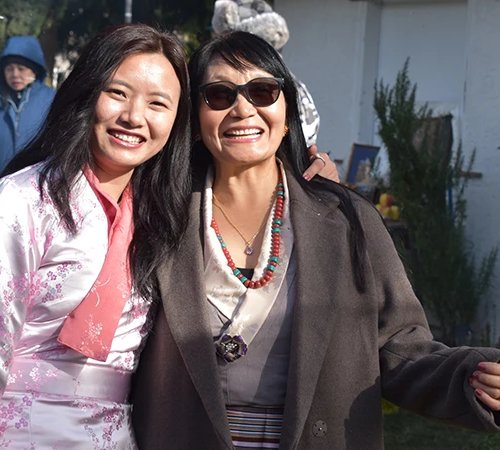 Two women smile warmly while wearing traditional clothing and jewelry. This personal connection with local people is a highlight of a Tibet cultural tour.