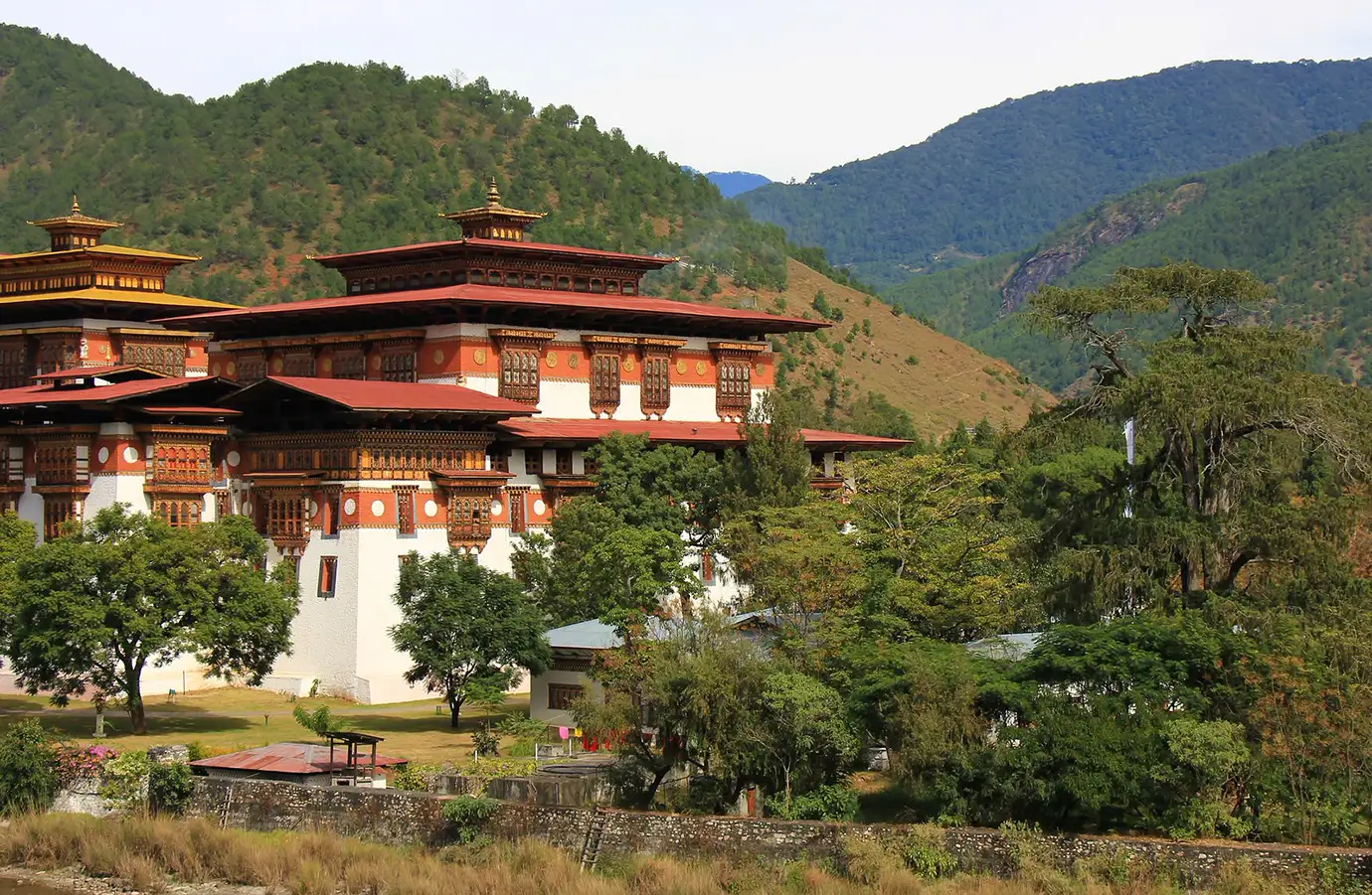 Traditional Bhutan Dzong surrounded by green hills and forest landscape, showcasing classic Bhutanese fortress architecture set within a peaceful Himalayan valley.