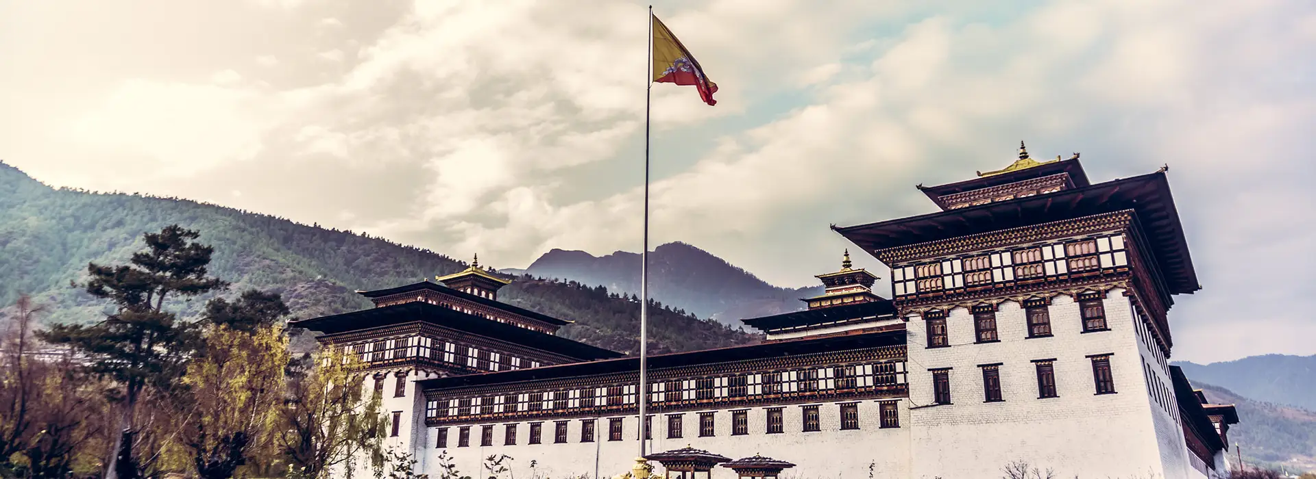 Historic Bhutan Dzong with national flag raised in the courtyard, surrounded by mountains, representing secure cultural sites that support Bhutan Travel Safety for visitors.