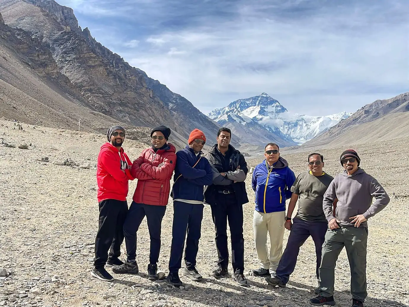Group of travelers standing on the rocky plateau near Everest Base Camp in Tibet with Mount Everest rising in the background during a Tibet adventure tour.