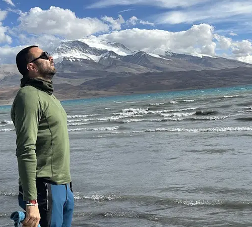 A traveler looks toward the snow-capped Himalayan peaks across a vast blue lake. This breathtaking scenery is a centerpiece of a Tibet tour from the USA.