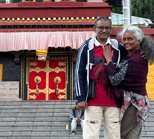 A smiling couple poses in front of a traditional yellow temple with red doors, capturing a memorable moment during their Tibet Tour Itinerary for First-Time Visitors.
