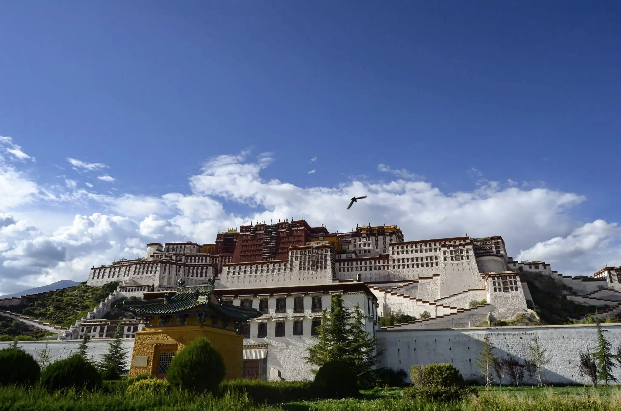 Potala Palace in Lhasa under a bright blue sky with clouds, gardens, and white monastery walls in the foreground