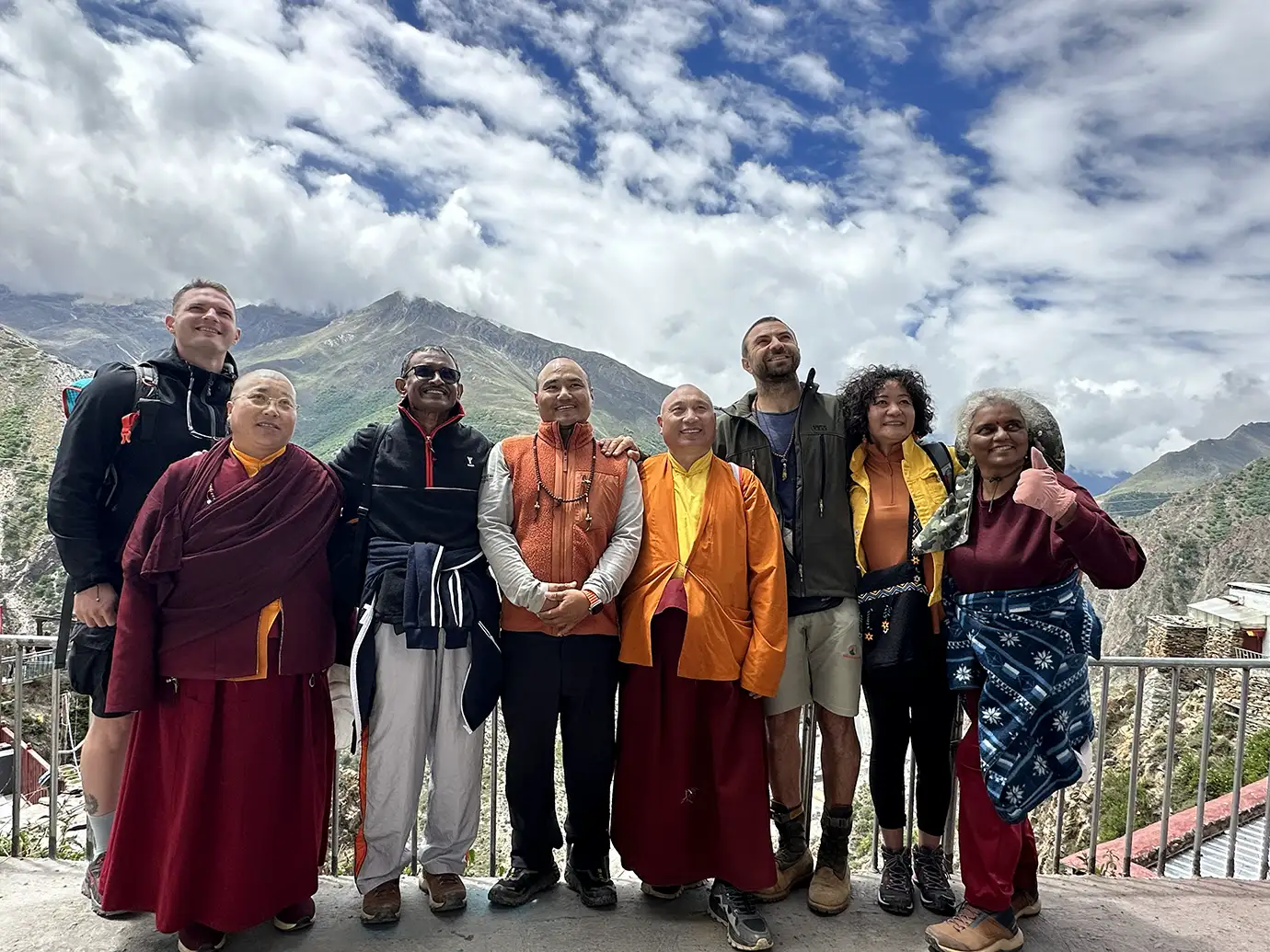 Travelers and monks stand together during a Tibet Private Tour vs Group Tour visit, with mountain views and a monastery setting in the background.