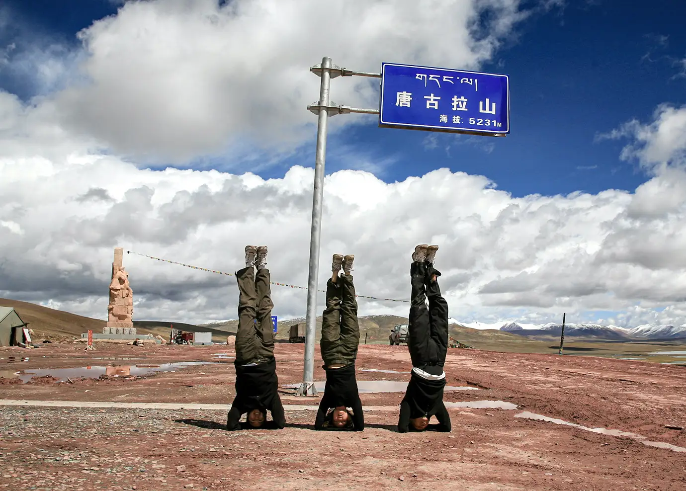 Three travelers perform headstands near a sign marking Tanggula Pass at 5,231 meters, a dramatic stop often seen during a Tibet tour by train across the high Tibetan Plateau.