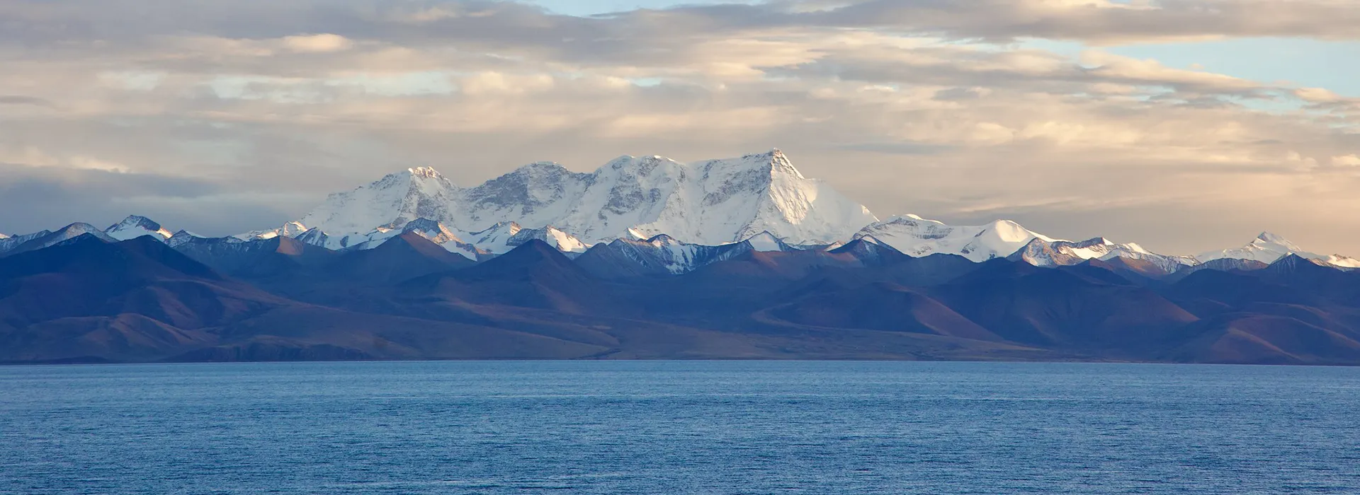 Snow-capped Himalayan peaks reflect over the deep blue waters of a sacred lake, a highlight of a Tibet Tour from Australia.