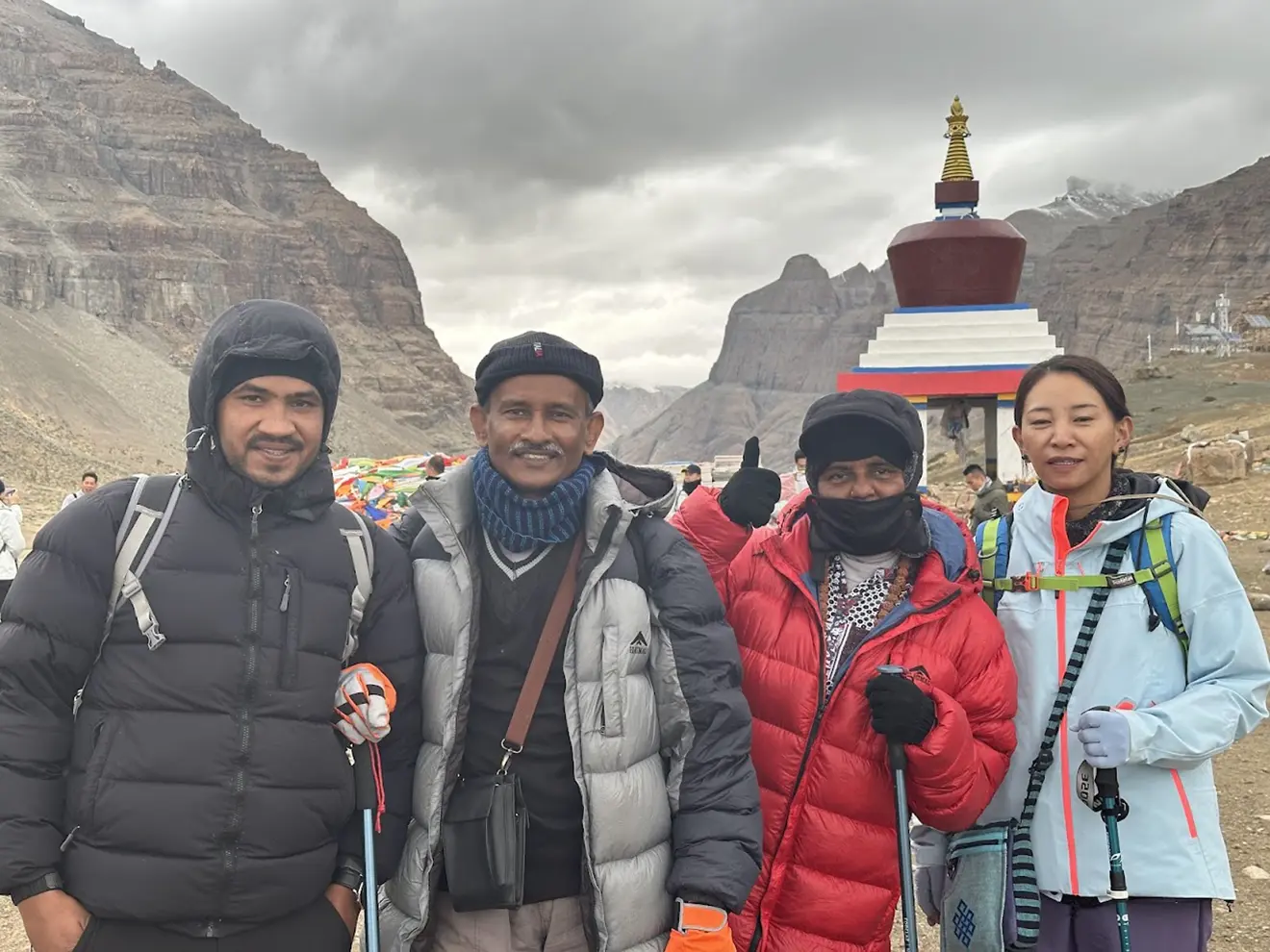 Four travelers in warm trekking gear stand together near a traditional stupa in a mountain valley during a Tibet tour from the UK.