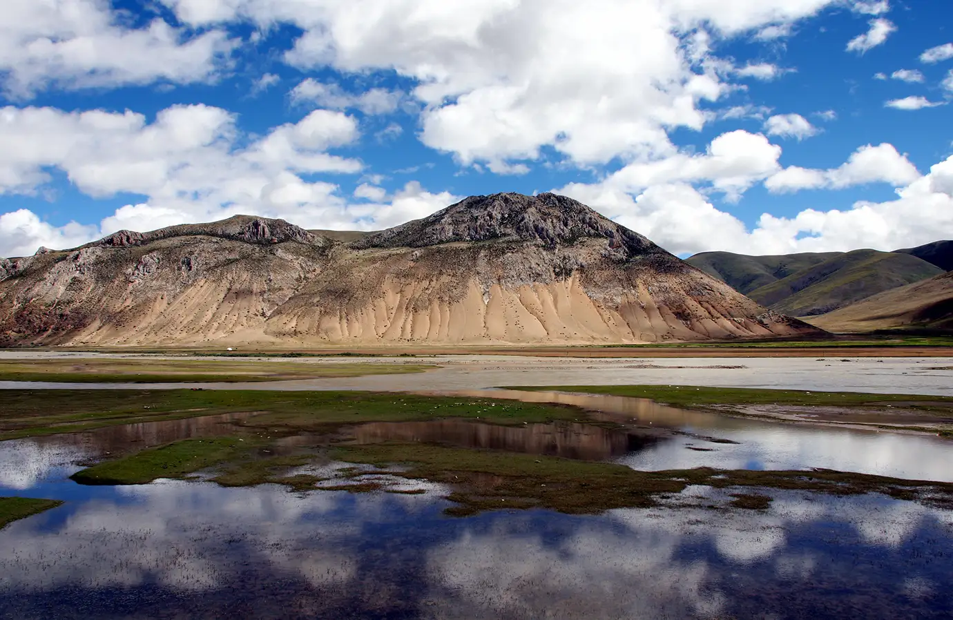 Wide alpine landscape with a reflective lake and rugged mountains on the Tibetan Plateau, a scenic view travelers often see during a Tibet tour by train across western China.