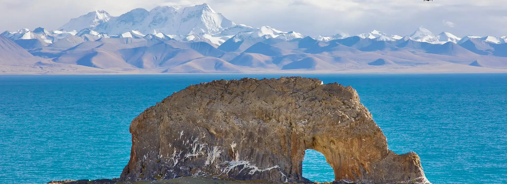 A large rock formation shaped like an elephant stands before turquoise waters and snow-capped peaks, a scenic stop on a Tibet Tour Itinerary for First-Time Visitors.