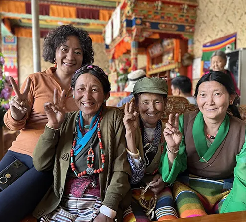 Four smiling women gesture with peace signs inside a colorful traditional teahouse. Visiting these local social hubs requires a valid Tibet travel permit.