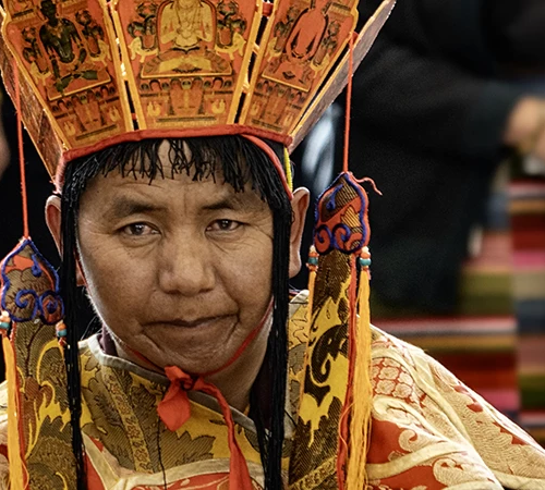 A Tibetan monk wearing an ornate Five-Buddha crown and traditional ceremonial robes prepares for a sacred ritual during a vibrant Tibet festival.