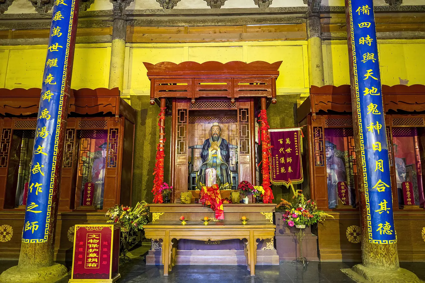 Decorated shrine with a seated spiritual statue inside a traditional temple hall visited during a Tibet spiritual tour, surrounded by colorful banners, offerings, and carved wooden architecture.