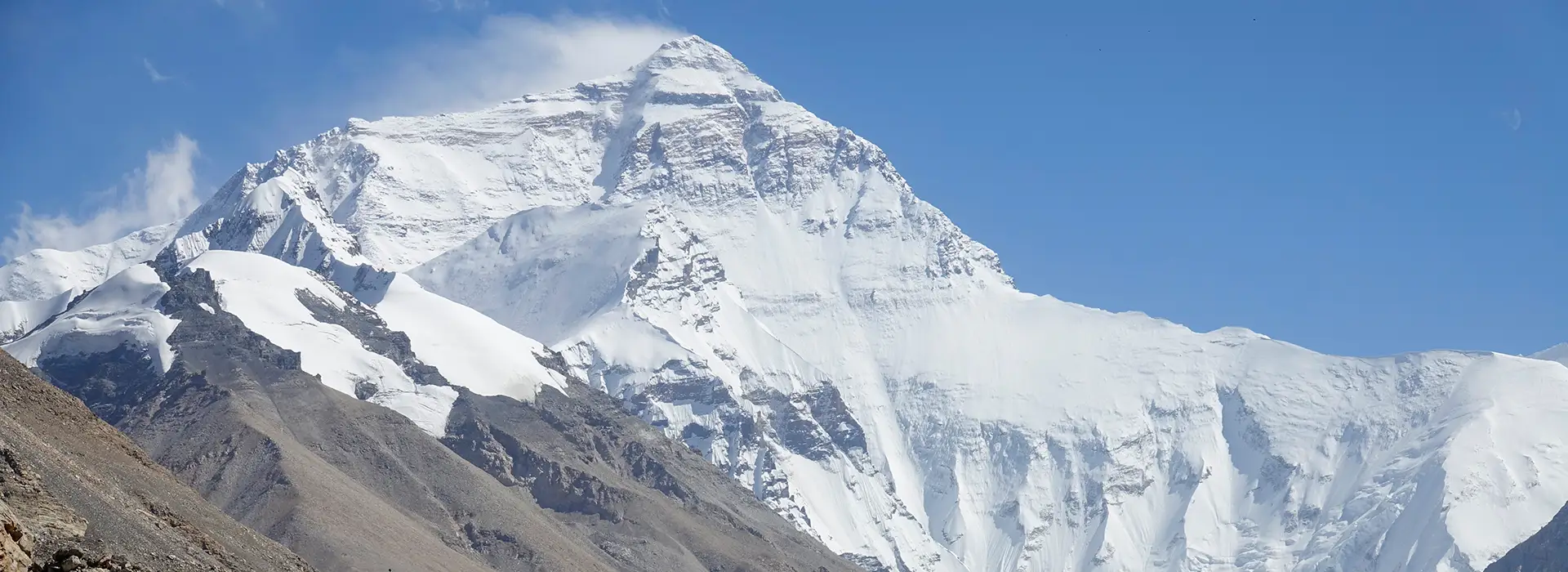 Mount Everest rises above the Tibetan plateau with massive snow-covered slopes and a clear blue sky, a major highlight for travelers on a Tibet Tour from Singapore.