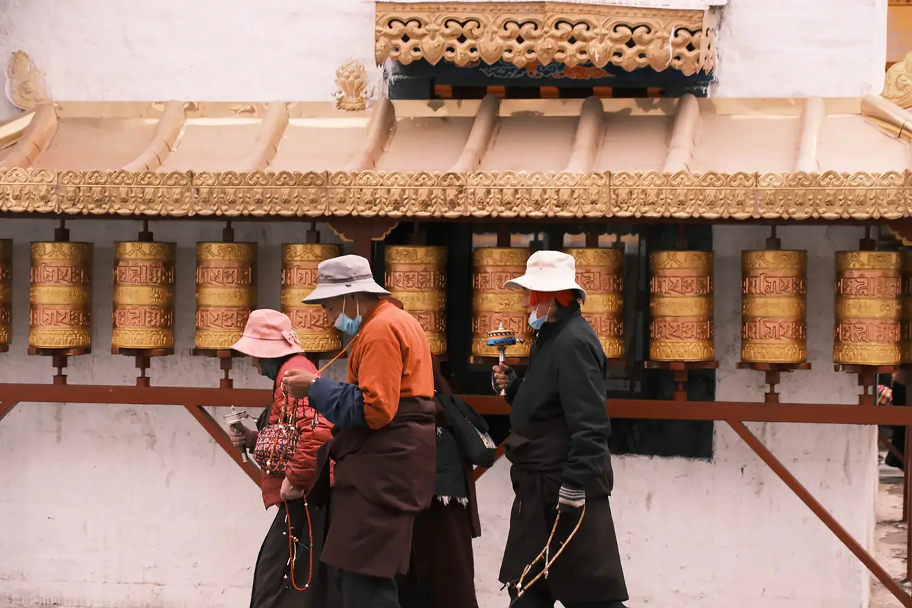Devout pilgrims carrying prayer wheels walk past a long row of golden spinning cylinders in Lhasa during a traditional Tibet festival celebration.