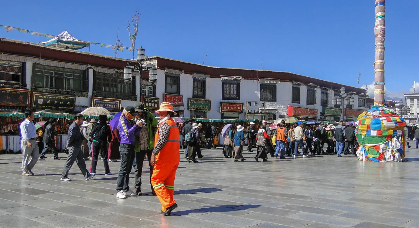 Travelers and locals walk through a sunny Barkhor Street square in Lhasa, a vibrant cultural hub often visited during a Tibet Tour from Australia.