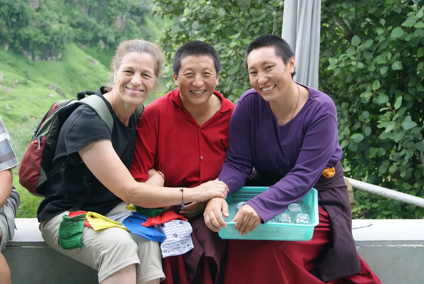 Traveler shares a friendly moment with two local women during a Tibet Private Tour vs Group Tour experience in a green hillside setting.