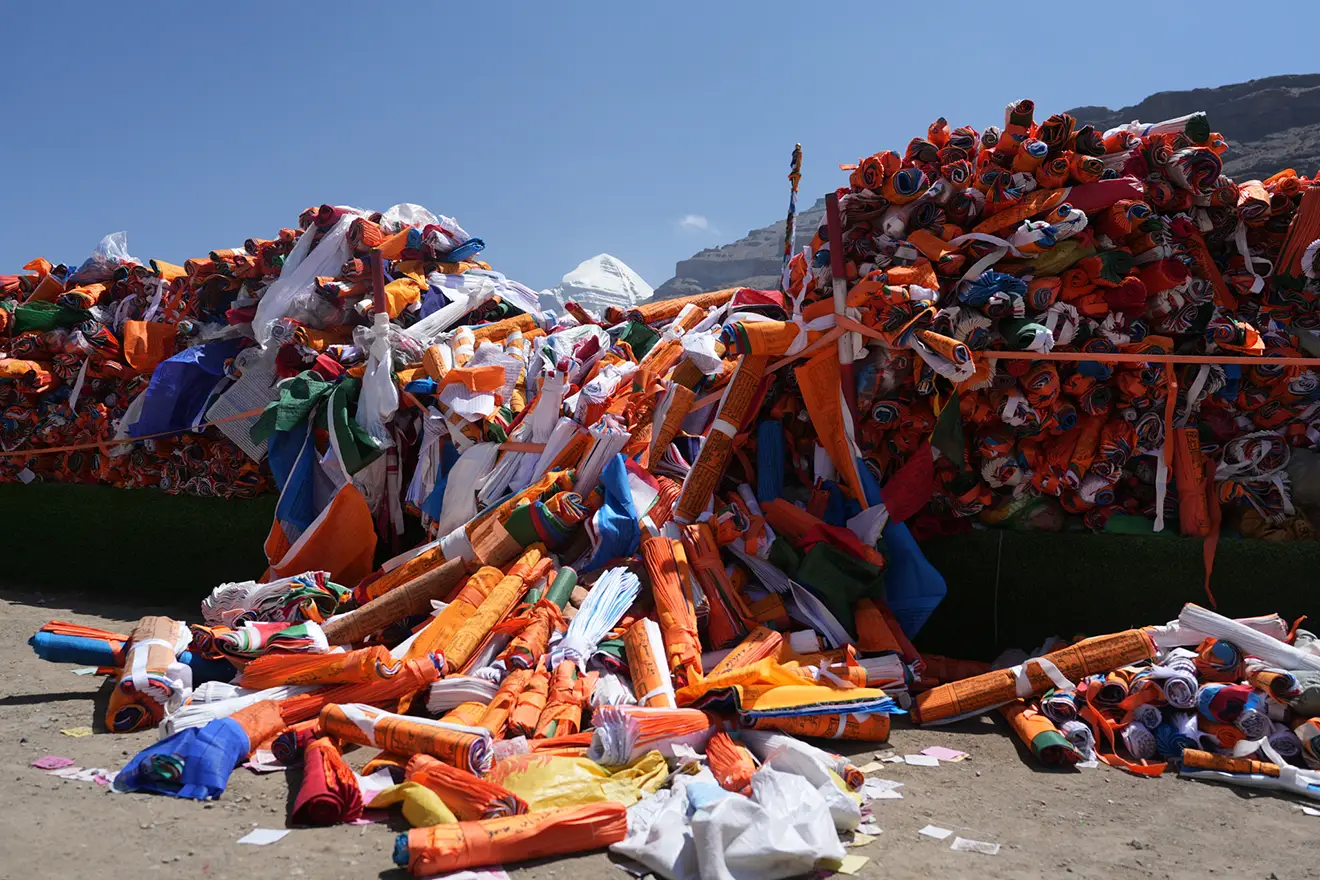 Piles of colorful rolled prayer flags and scriptures sit before the distant peak of Mount Kailash during a sacred Tibet festival celebration.