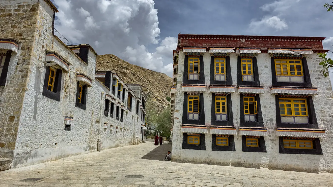Traditional white stone buildings with yellow window frames at Sera Monastery in Lhasa. Visitors often research Tibet tour cost before visiting this historic monastic site.