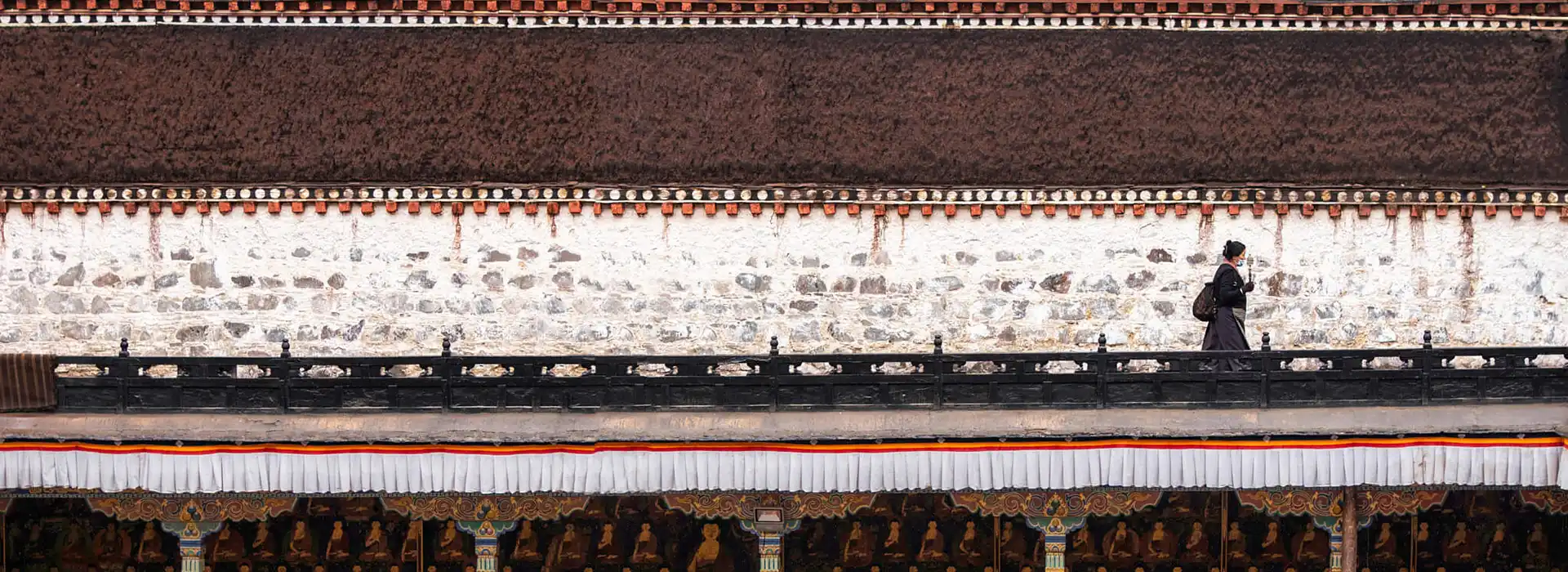 A woman walks along a high balcony of a traditional Tibetan monastery. Visitors must carry a valid Tibet travel permit to explore this historic site.