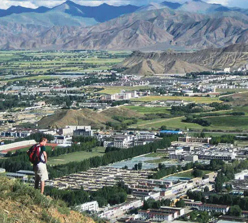 Traveler stands on a hill overlooking Lhasa city and the surrounding Tibetan valley during a Tibet Tour from Singapore.