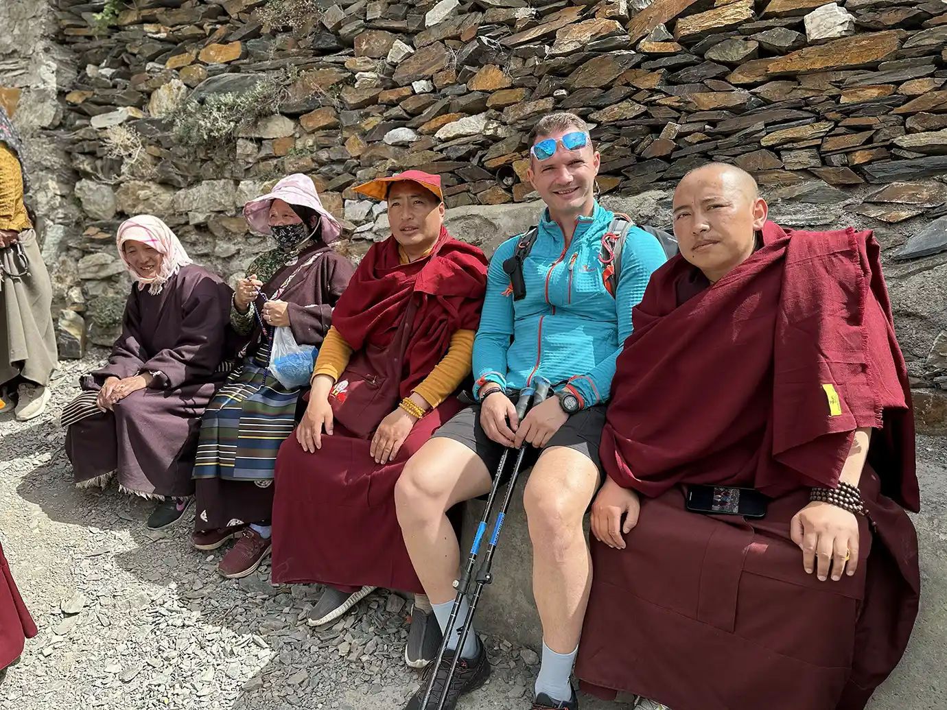 Traveler sitting with local residents and monks during a Tibet Private Tour vs Group Tour experience, showing direct cultural contact in a relaxed mountain setting.