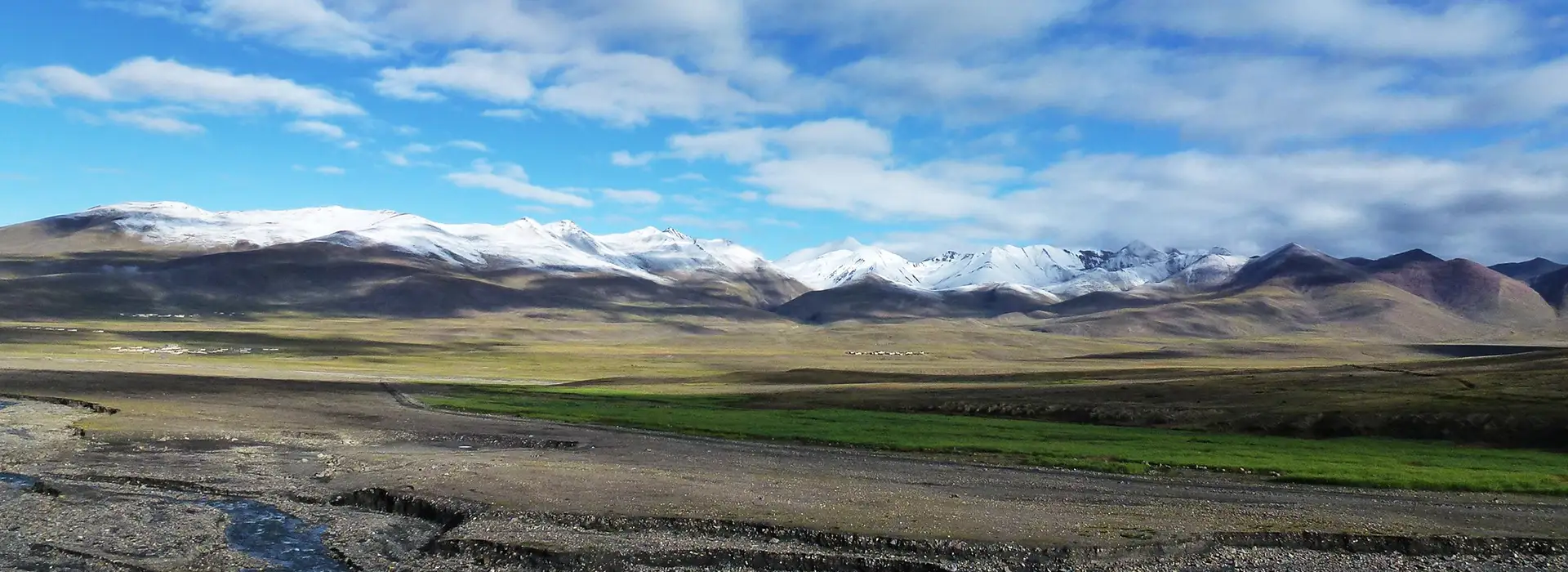 A hiker with a backpack and walking pole stands before a sweeping vista of snow-capped peaks and rolling high-altitude plains. Selecting the best time to visit Tibet is key to experiencing these clear mountain views.
