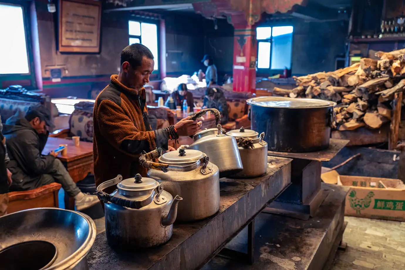 A man prepares traditional sweet tea in large metal kettles within a rustic Lhasa teahouse, a culturally rich activity for any Tibet Tour Itinerary for First-Time Visitors.