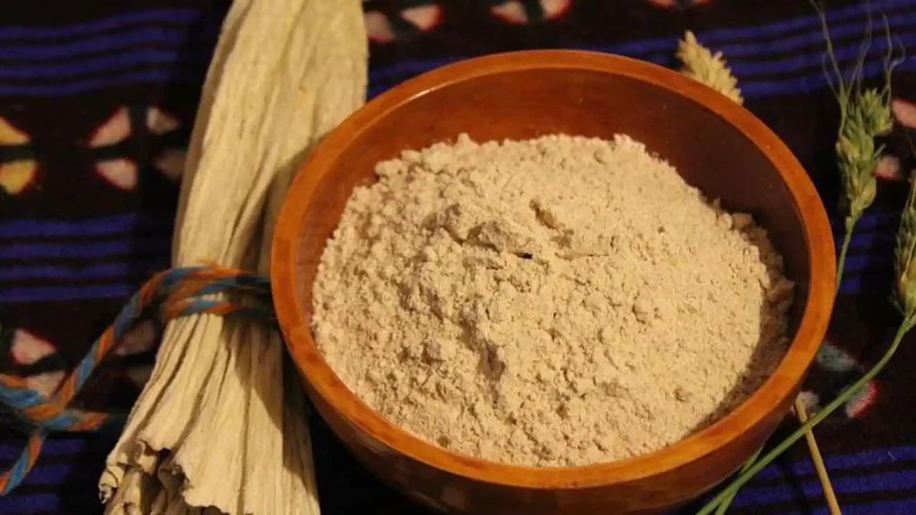 A wooden bowl filled with Tsampa (roasted barley flour) sits next to a bundle of traditional textiles. Sampling local staples is a must, regardless of the best time to visit Tibet.