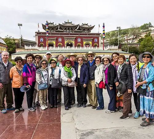 Group of travelers standing in front of a traditional Tibetan monastery during a Tibet spiritual tour, visiting sacred Buddhist sites and learning about Tibetan culture and religious heritage.