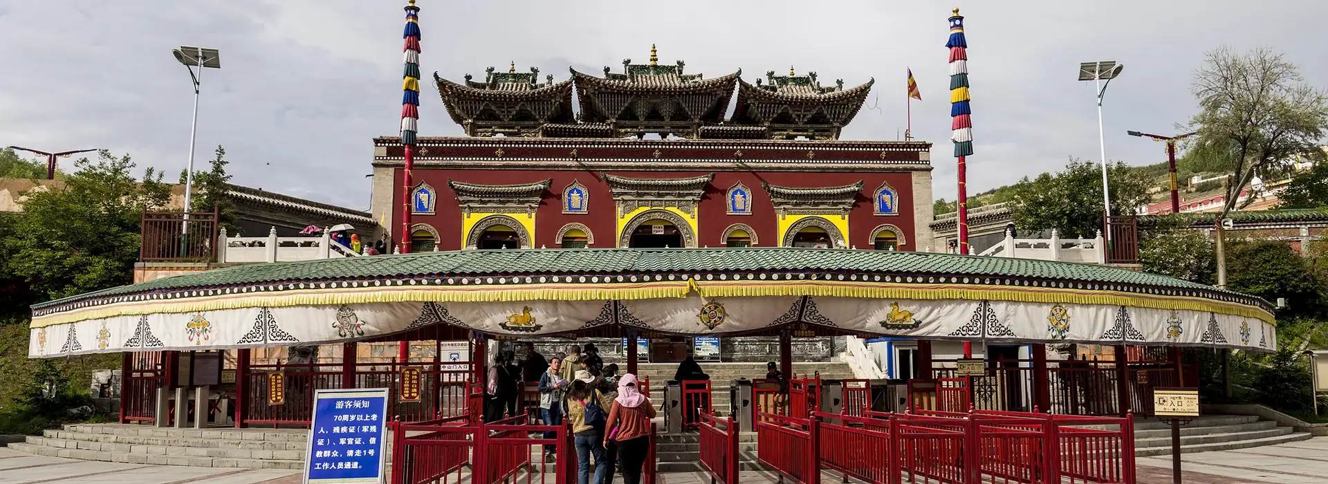 Travelers enter a colorful Tibetan monastery complex with ornate roofs and prayer pillars during a Tibet tour by train, exploring historic Buddhist sites after arriving in Lhasa.