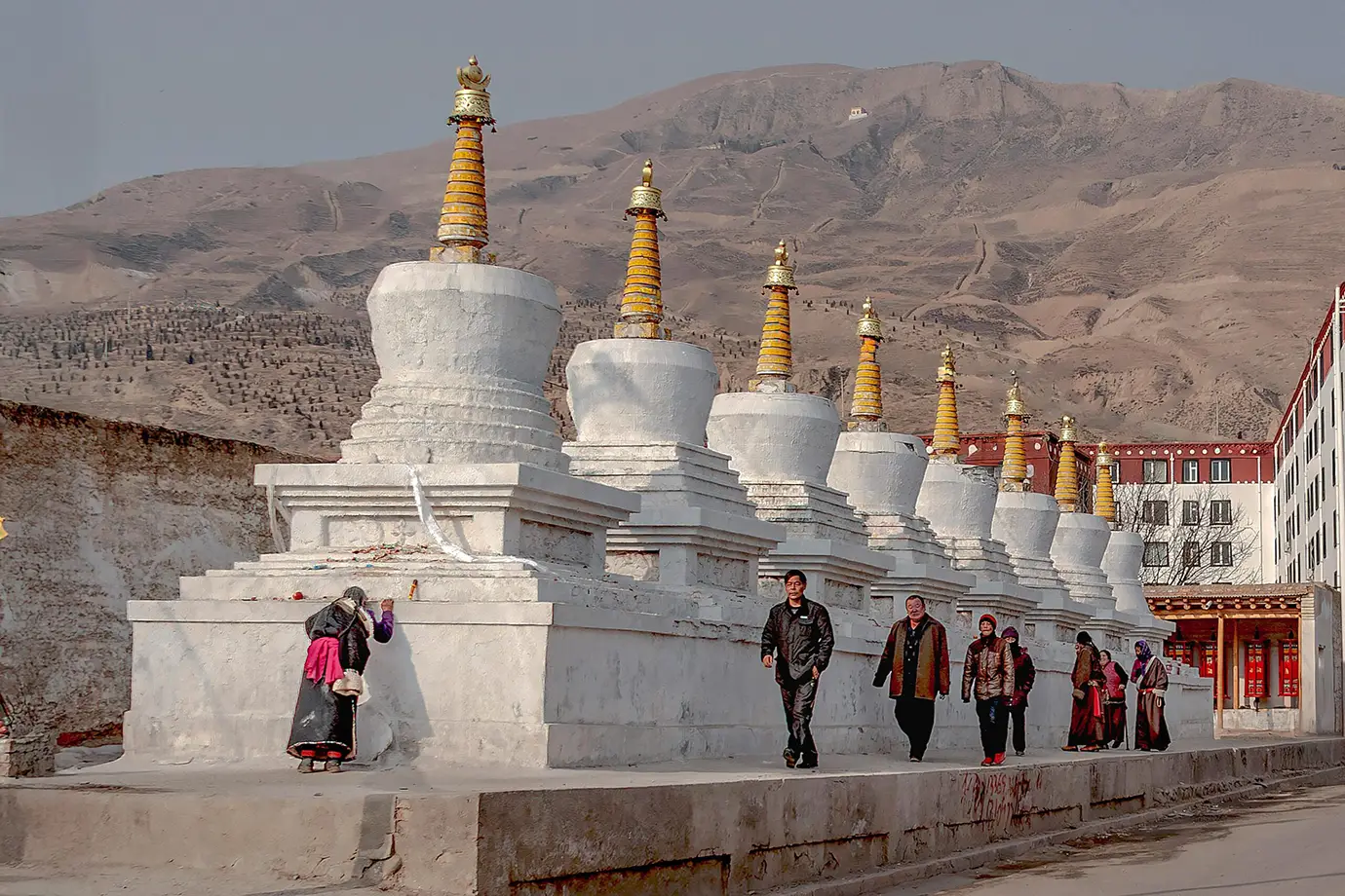 Visitors walk beside white Tibetan stupas in Lhasa, showing how Tibet travel restrictions still shape access, movement, and sightseeing across important cultural areas.