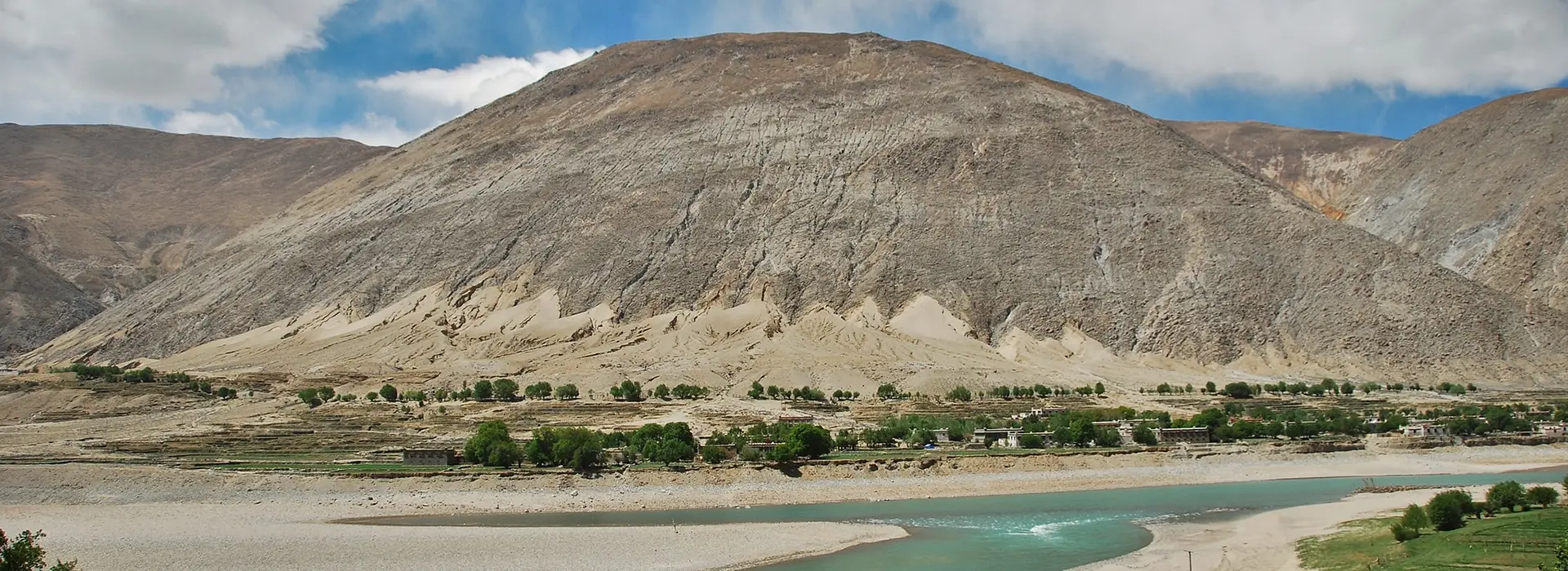 A remote Tibetan valley with a river, sparse settlement, and dry mountain slopes reflects how Tibet travel restrictions can affect route access and regional movement.