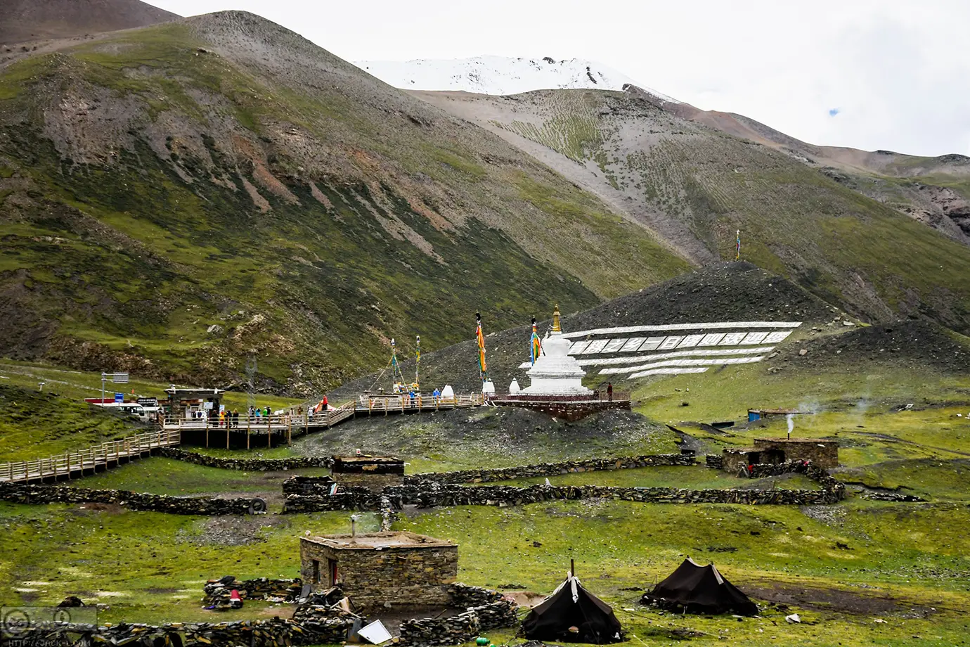 A remote high-altitude site in Tibet with prayer flags, small structures, and mountain slopes shows how Tibet travel restrictions can affect access to isolated areas.